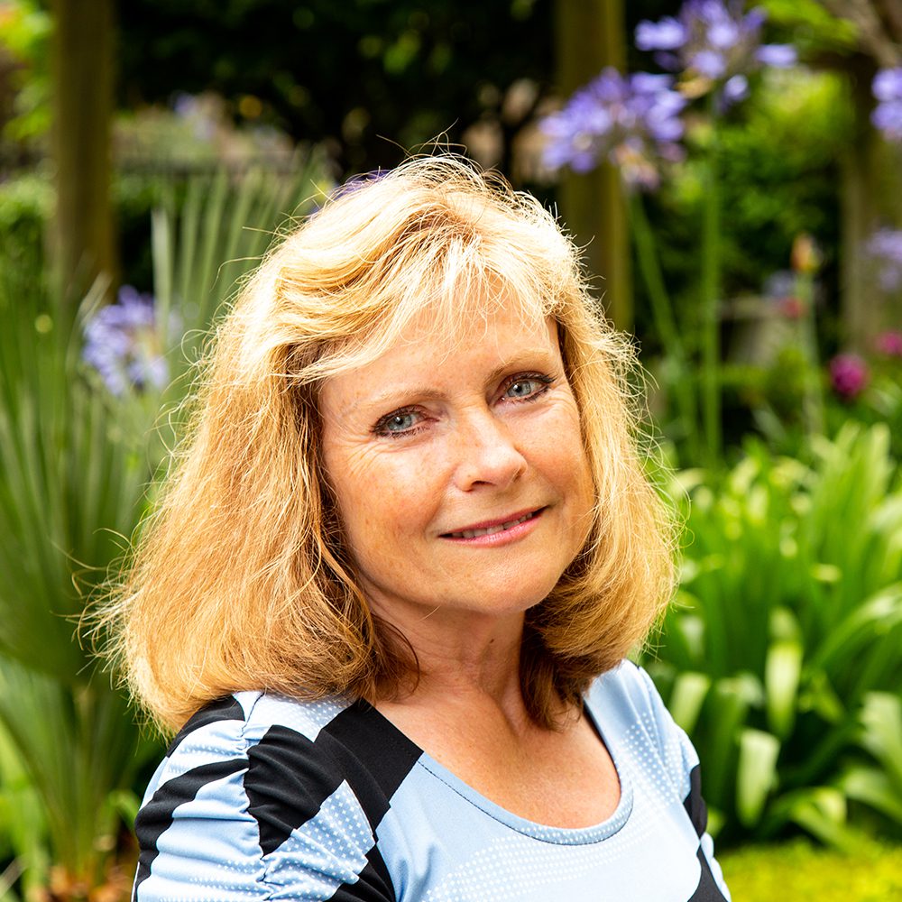 Woman with blonde hair smiling in a garden.