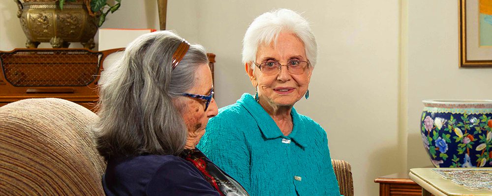 Two senior women smiling while sitting.