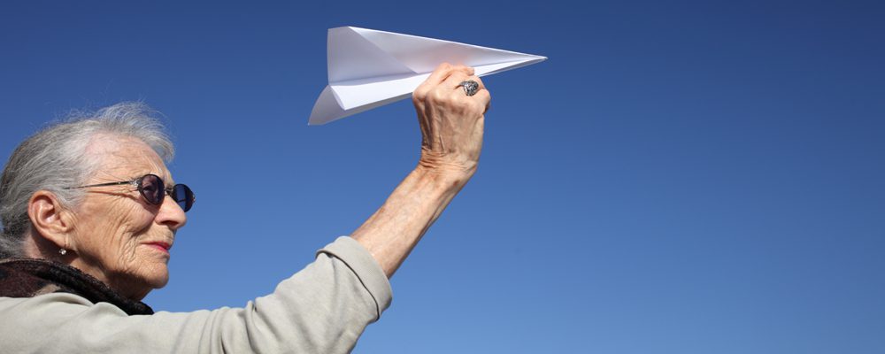 Senior woman launching a paper airplane.