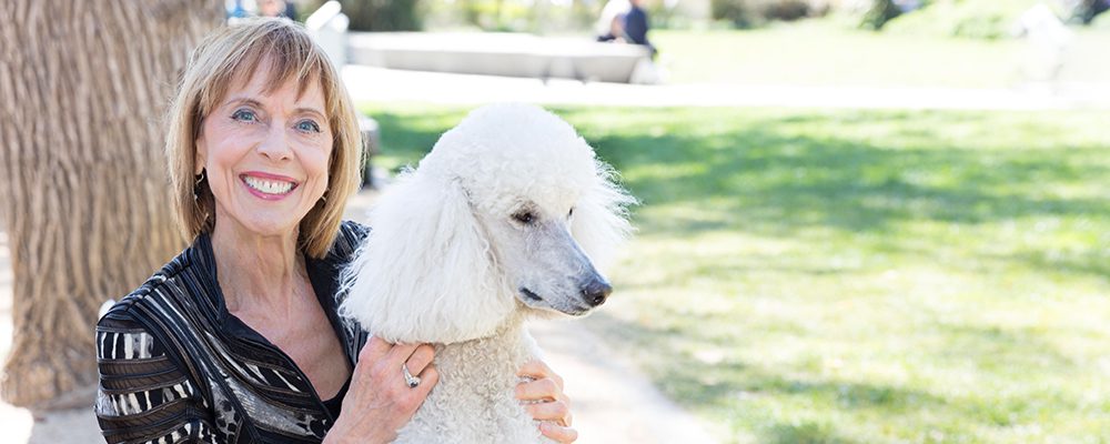 Woman smiling, petting white poodle.